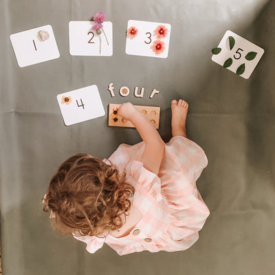 An adorable little girl doing Charlotte mason activities and play based learning with a wooden ten frame for preschool math.